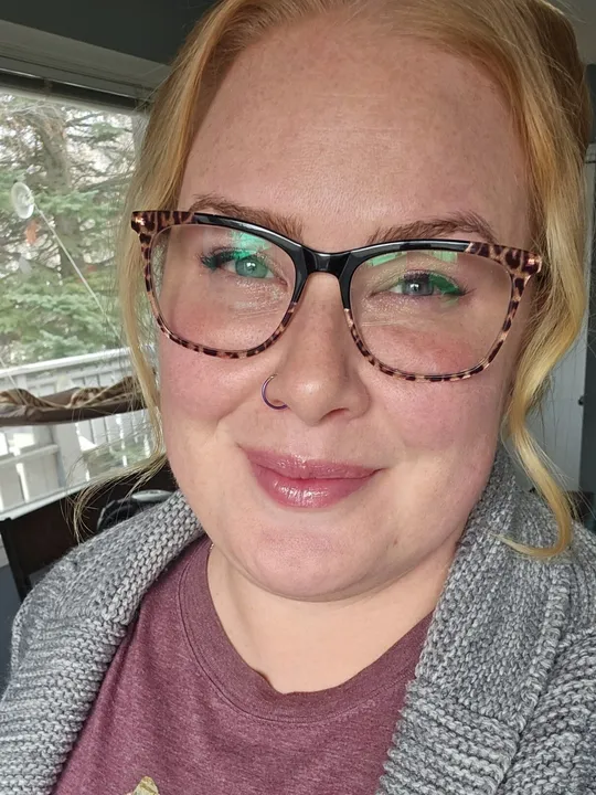 Cassaundra, a blonde woman wearing glasses, smiling in a casual selfie taken indoors.
