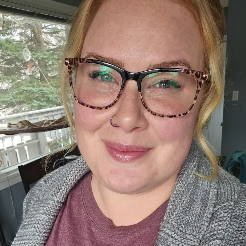 Cassaundra, a blonde woman wearing glasses, smiling in a casual selfie taken indoors.